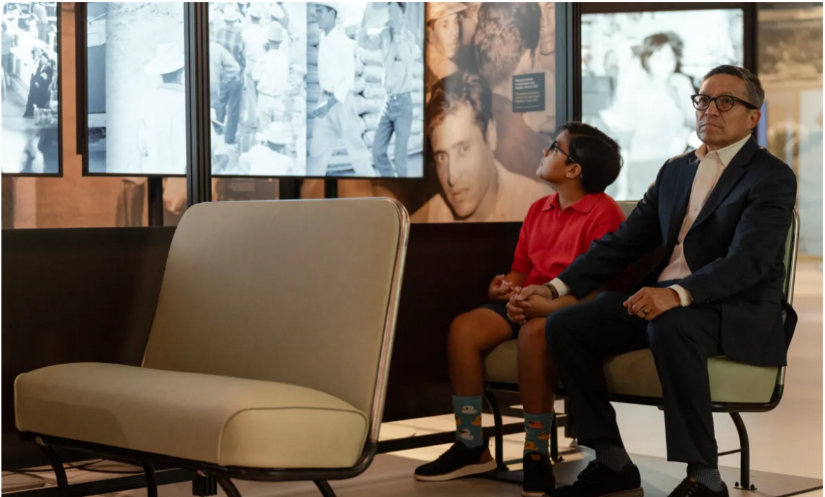 Left to right, 10-year-old Nicolás holds father Pablo Espinoza’s hand as they watch a video from bus seats at the new “Help Wanted/ Leave Now” exhibit at the California Museum in Sacramento on Aug. 12, 2026.